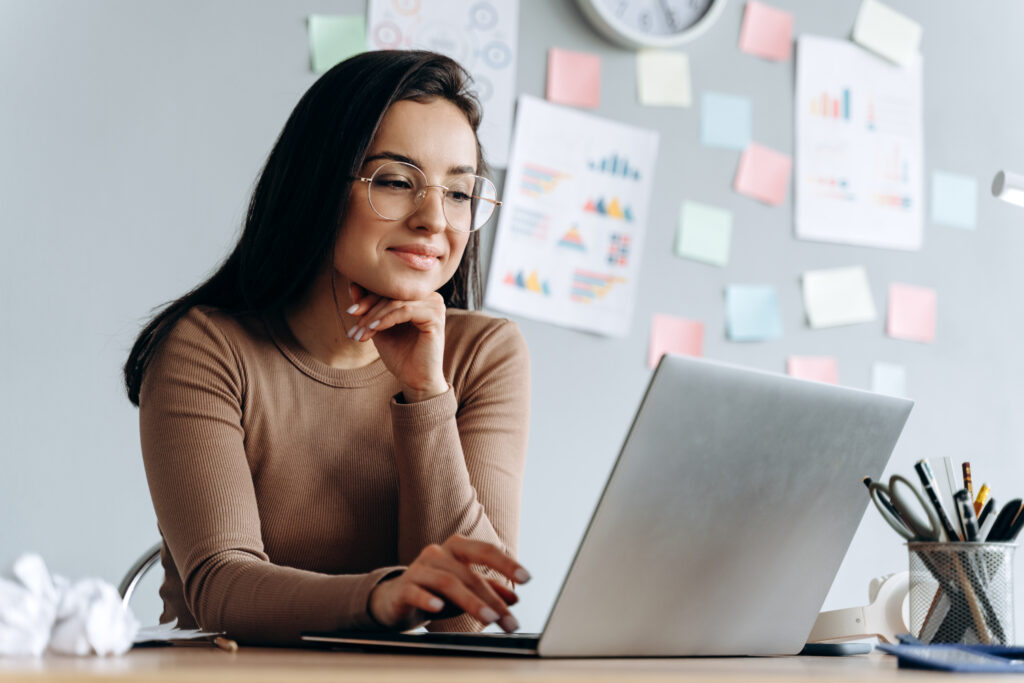  Uma mulher está utilizando um notebook para fazer a gestão de pessoas de TI e ponderando sobre terceirizar o time de TI.
