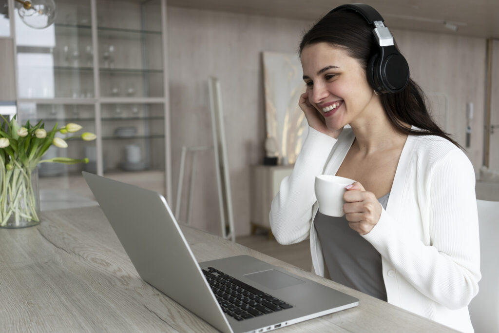 Uma mulher sorridente está na sala da sua casa, trabalhando com notebook e headset, representando o fit cultural remoto.