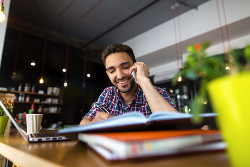 Um homem durante um programa de Learning Experience Design (LXD). Ele fala ao celular enquanto verifica algumas informações em um livro.