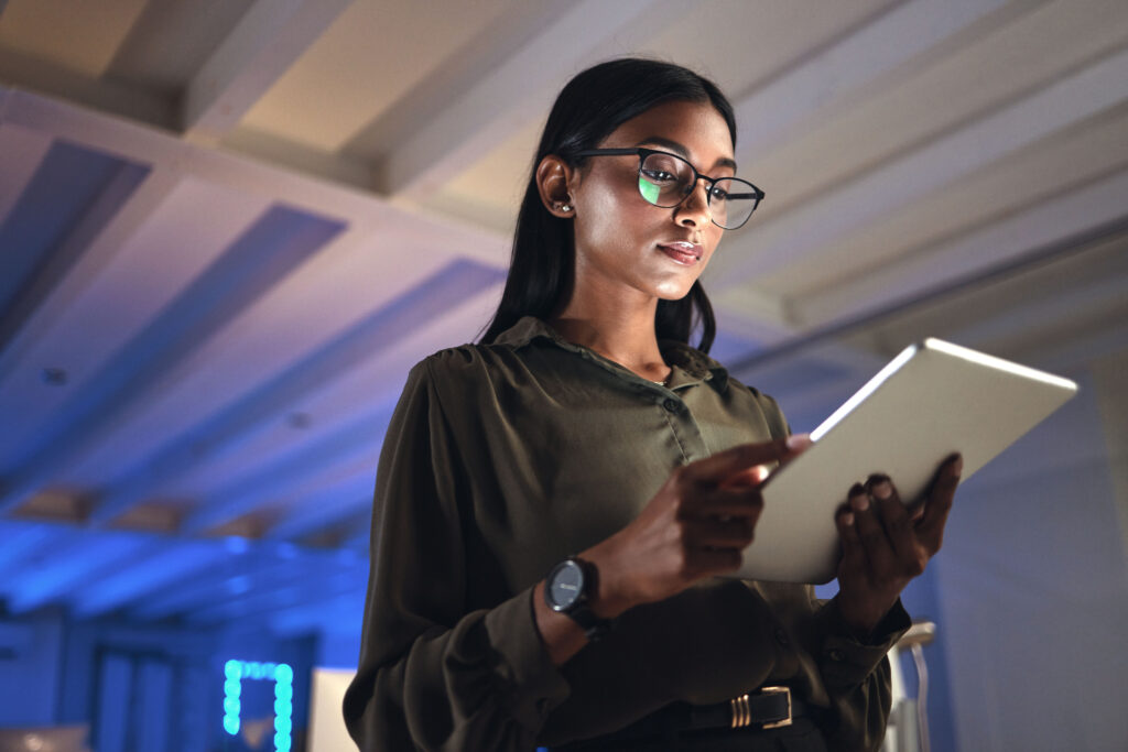 Habilidades essenciais para profissionais de TI 1 Mulher utilizando um tablet em um ambiente corporativo, representando os profissionais de TI e suas habilidades.