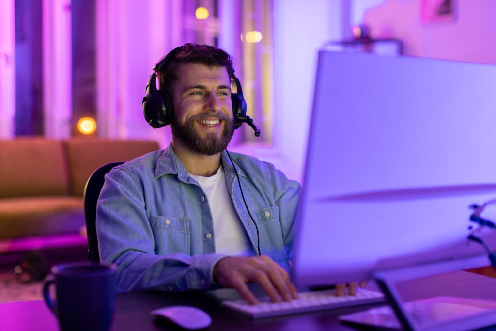 Profissional de SRE sorridente, enquanto trabalha em um computador, usando fones de ouvido headset.