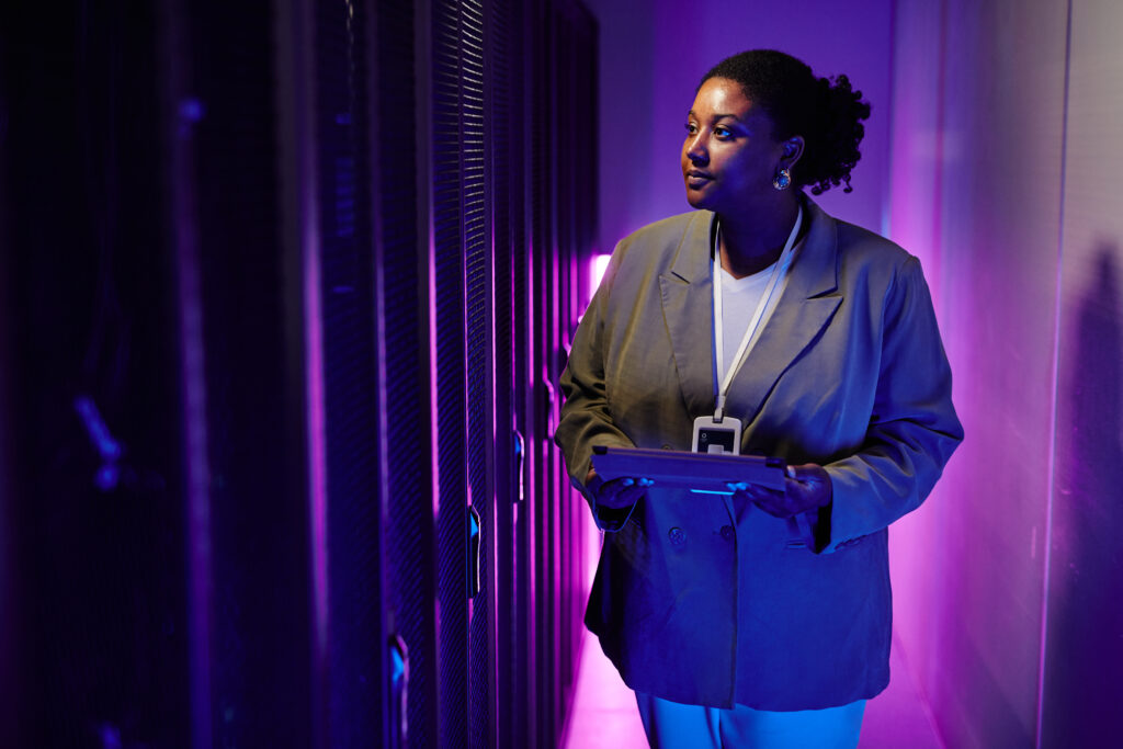 Uma colaboradora contratada através do modelo de body shop de TI está em um data center segurando um tablet.