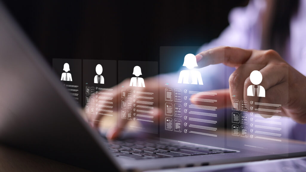 Uma pessoa utiliza um notebook, enquanto seleciona perfis de algumas pessoas em uma tela holográfica, representando o que é um techrecruiter.