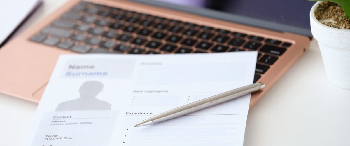 Ballpoint pen lying on resume document for employment near laptop closeup. Job search online concept