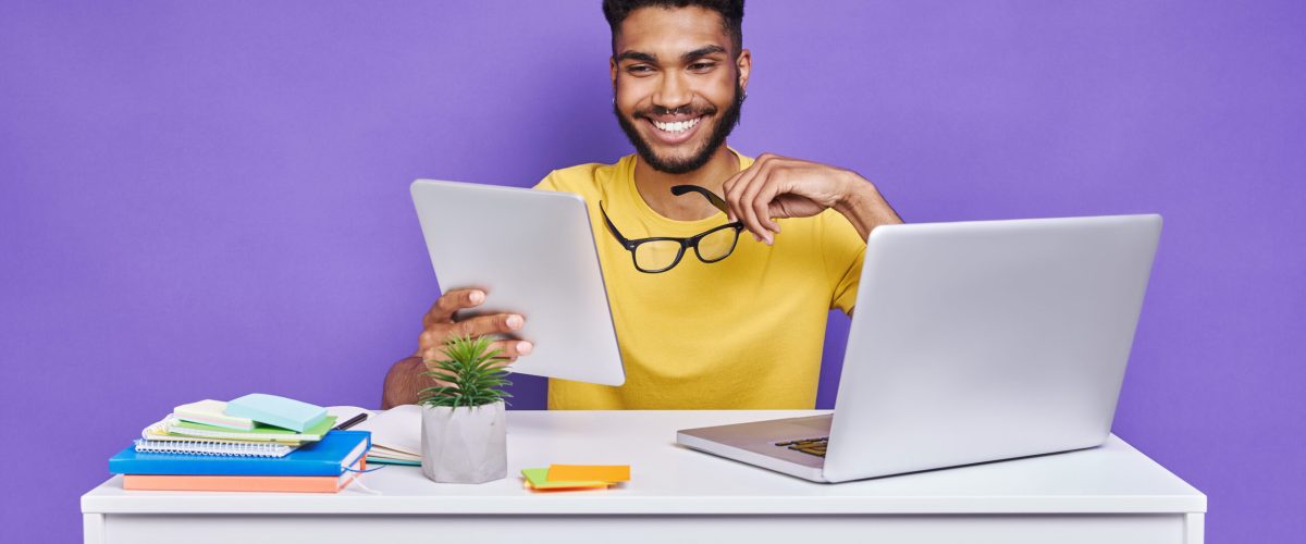 Happy African man using digital tablet while sitting at the desk against purple background