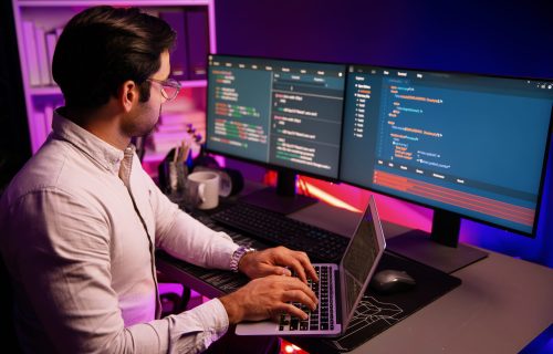 Smart IT developer working on laptop to type searching in software coding system at neon light office room, creating application program update latest version online website database online. Surmise.