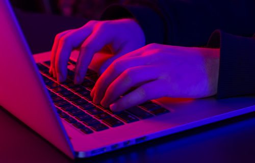 A man uses a laptop, close-up, male hands in neon lighting, the concept of working at night.