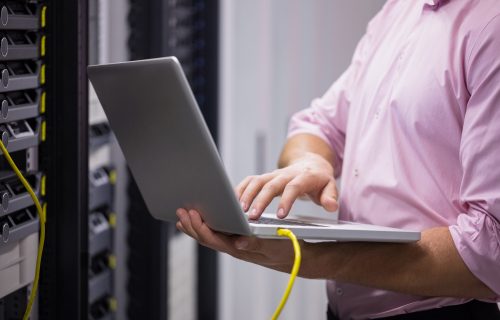 Mid section of a technician typing on his notebook in large data center