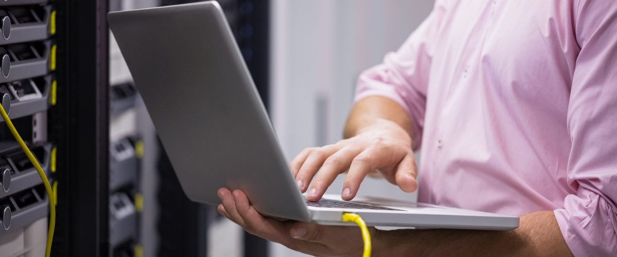 Mid section of a technician typing on his notebook in large data center