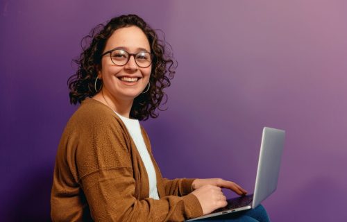 Woman wearing glasses smile to a camera with a laptop background happy electronics.