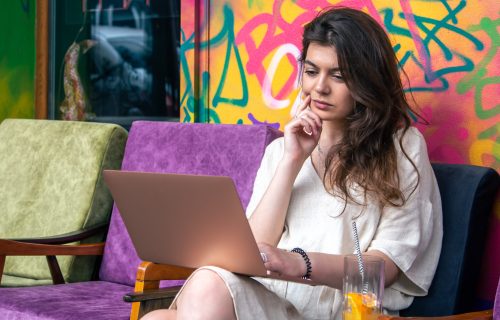 Attractive young woman working on a laptop in the summer outdoors on the terrace of a cafe.