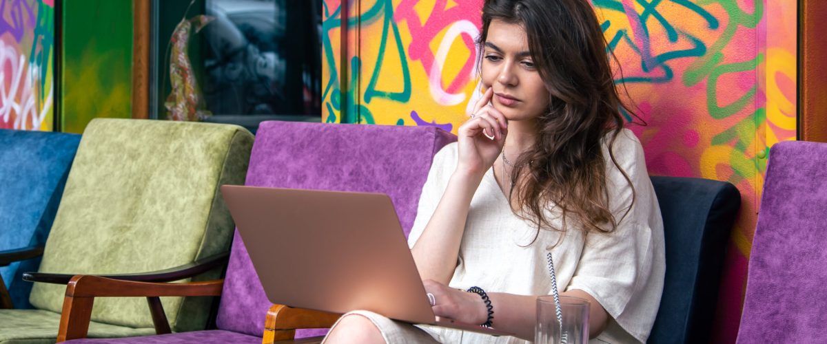 Attractive young woman working on a laptop in the summer outdoors on the terrace of a cafe.